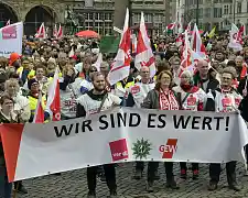 Viele Personen, die am Warnstreik teilnehmen, halten einen Banner Wir sind es wert!