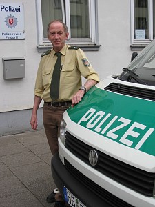 Das Bild zeigt Heinz-Georg Niemann vor seinem Revier an einem Polizeiwagen stehend.