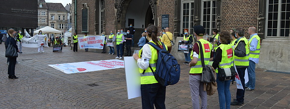 Etwa 30 Personen stehen im Halbkreis . Auf dem Boden ist ein Transparent ausgebreitet.