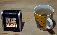Ein Becher mit Tee auf einem Tisch. Daneben steht eine Uhr mit Temperaturanzeige. Sie zeigt 21:52 Uhr und 10,3 Grad