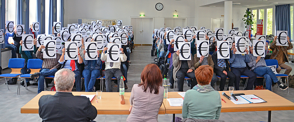 TeilnehmerInnen halten sich ein Blatt mit einem Euro-Zeichen vor das Gesicht