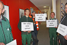 Auszubildende stehen mit Schildern im Flur vor den geschlossenen Türen einer Betriebsausschusssitzung