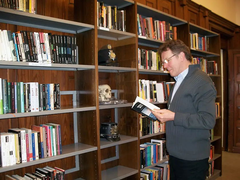 Kollege Bernd Krause steht lesend vor einem Bücherregal