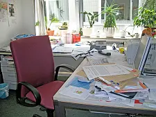 unaufgeräumter Schreibtisch mit Stuhl, an dem keiner sitzt