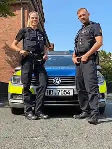 Polizistin und Polizist vor ihrem Polizeiauto