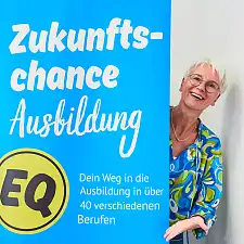 Sandra von Atens schaut hinter einem Werbeaufsteller des Programms Zukunftschance Ausbildung hervor