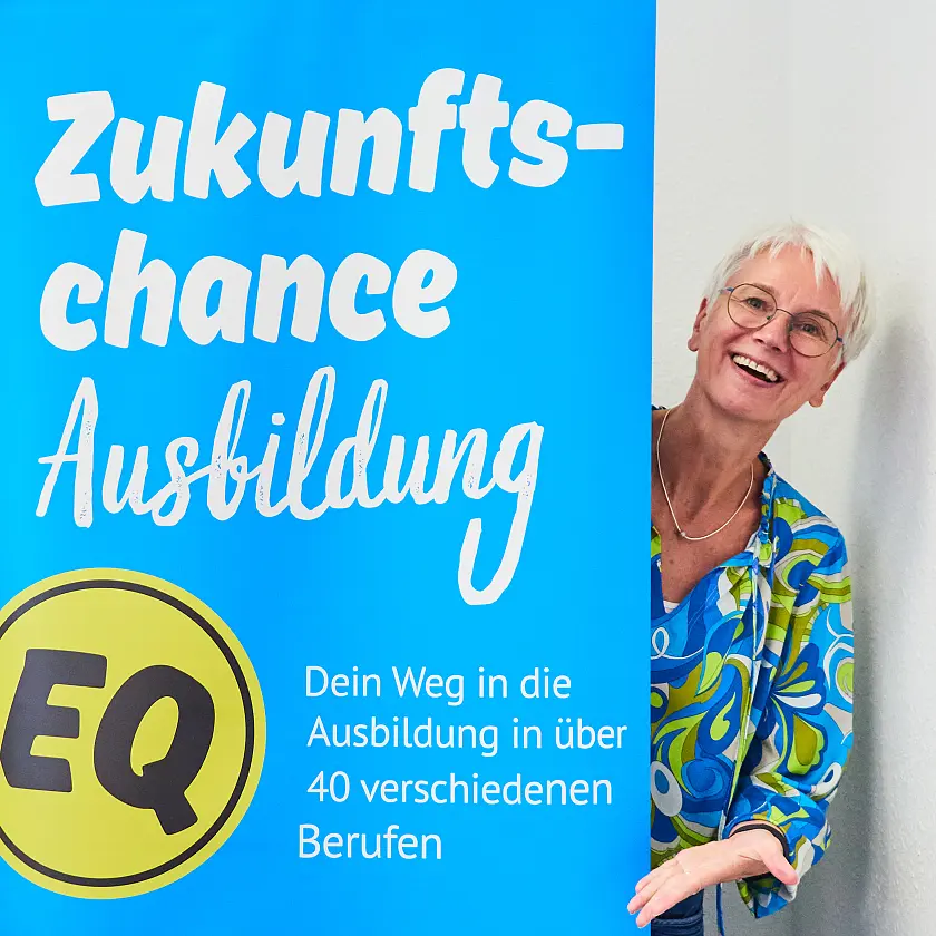 Sandra von Atens schaut hinter einem Werbeaufsteller des Programms Zukunftschance Ausbildung hervor