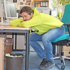 Ein junger Mann, der mit dem Oberkörper auf seinen Schreibtisch gesunken ist.