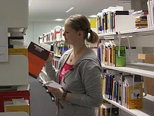 Fachangestellte für Medien- und Informationsdienste steht vor einem Bücherregal