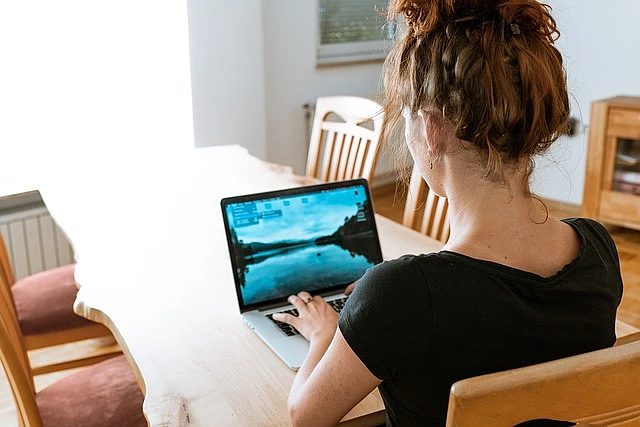 Eine Frau arbeitet am Esszimmertisch an ihrem Notebook.